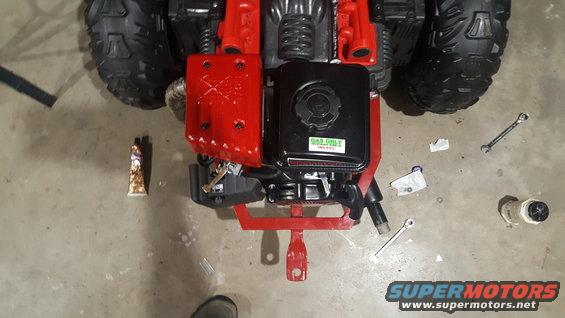 Small engine with red cover and black gas tank, tools and a tube of sealant on concrete floor