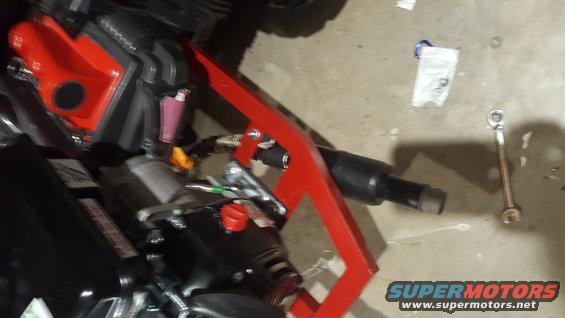 Close-up of a red bracket attached to a black engine component, with tools on the floor