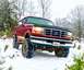 1995 Ford Bronco - A red Ford Bronco with a lifted suspension navigates through a snowy landscape.
