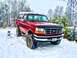 1995 Ford Bronco - A red 1995 Ford Bronco equipped with large off-road tires navigates a snowy landscape.