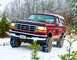 1995 Ford Bronco - Red 1995 Ford Bronco navigates a snowy, wooded area with its headlights on.