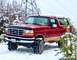1995 Ford Bronco - A red Ford Bronco is parked in a snowy landscape with trees and a power line tower in the background.