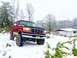 1995 Ford Bronco - Red 1995 Ford Bronco sits in the snow, surrounded by bare trees and a white building.