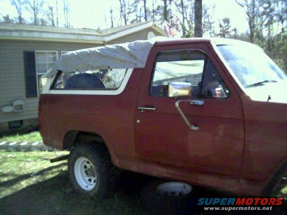 1986 Ford Bronco side view, red paint, tarp covering the roof and rear