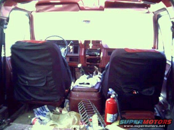 Interior of a 1986 Ford Bronco with seat covers, a fire extinguisher, and various items on the floor