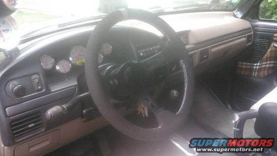 1992 Ford Bronco interior with aftermarket steering wheel, multiple gauges on dashboard, and plaid seat cover