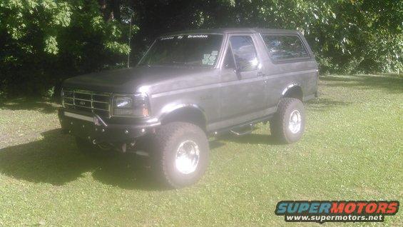 Lifted dark gray 1992 Ford Bronco with custom bumper and off-road tires parked on grass.