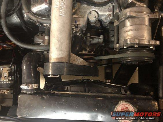 Close-up of engine bay showing a supercharger, belts, hoses, and radiator