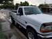 1995 Ford Bronco - This white pickup truck is parked on a wet street next to a sidewalk, with trees and houses in the background.