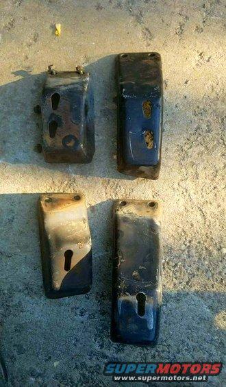 Four dark, rectangular metal brackets with keyhole slots and bolt holes, lying on a concrete surface