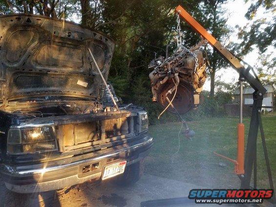 1995 Ford Bronco with hood open and engine removed by an engine hoist