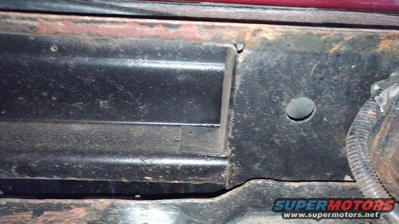 Close-up of a rusted metal frame section with a hole and wiring conduit