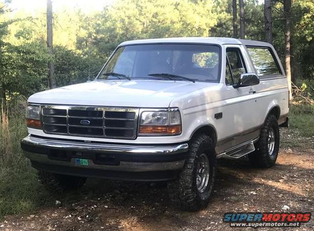 White 1996 Ford Bronco with chrome grille and aftermarket wheels parked on a dirt road