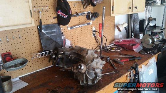 Transmission assembly on a workbench with tools and a grinder in the background