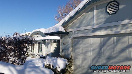 house with garage door covered in snow, icicles hanging from the roof, clear blue sky