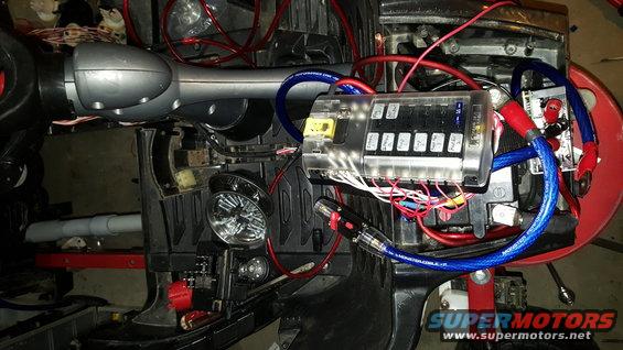 Close-up of a vehicle's fuse box and wiring harness with red and blue cables