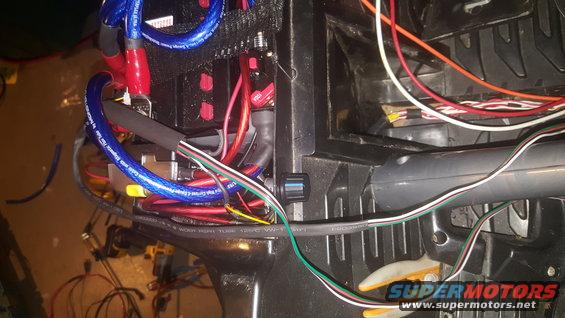 Close-up of vehicle wiring, battery terminals, and cables. Includes a Supermotors.net watermark