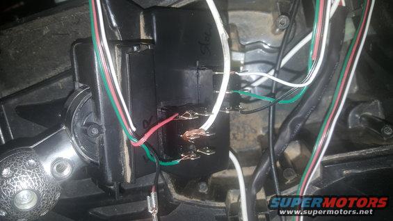 Close-up of a black electrical relay with multiple wires connected, some showing exposed copper. A silver textured knob is visible on the left