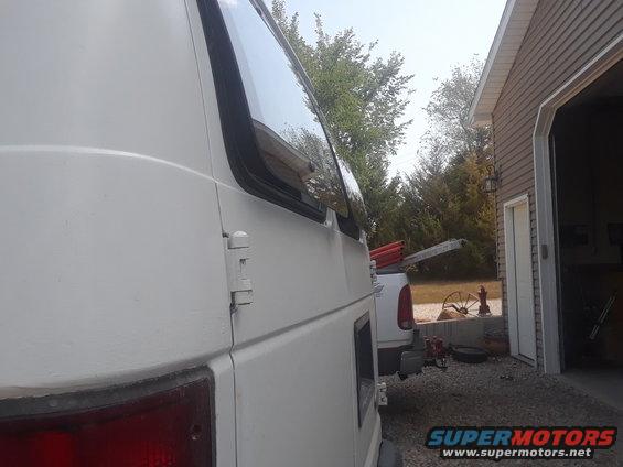 White 1999 Ford E250 van side view, parked next to a garage with a white pickup truck behind it
