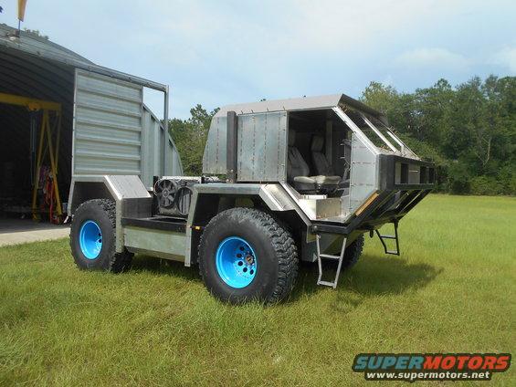 Custom off-road vehicle with blue wheels parked on grass near a large metal building