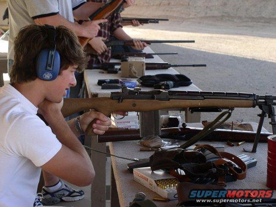 People at a shooting range aiming rifles. A box of Winchester ammunition is visible