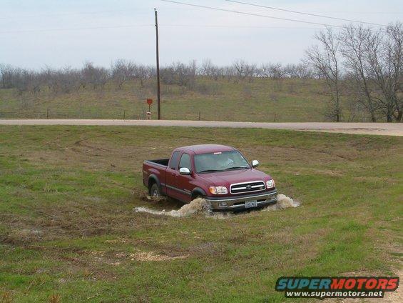Red Toyota Tundra pickup truck stuck in muddy ditch off a rural road