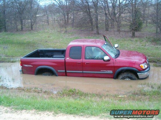Red Toyota Tundra stuck in a muddy ditch, driver's door open