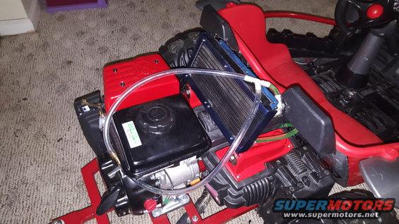 Red go-kart frame with black gas tank, engine, and blue radiator. Clear tubing connects components