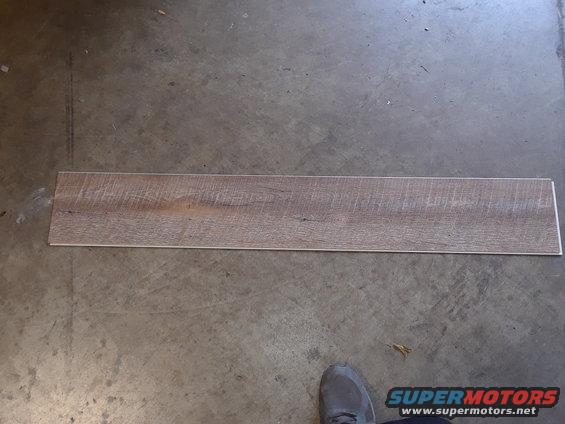 Wood-look plank on a concrete floor with a shoe in the lower right corner and Supermotors.net logo