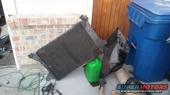 Radiator and some car parts are on the ground next to a trash can