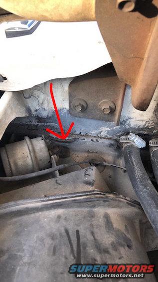 Close-up of engine bay with red arrow pointing to a seam, showing hoses and metal brackets