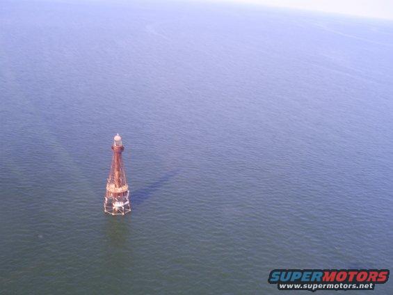 Lighthouse structure in the middle of the ocean, with a watermark for Supermotors.net