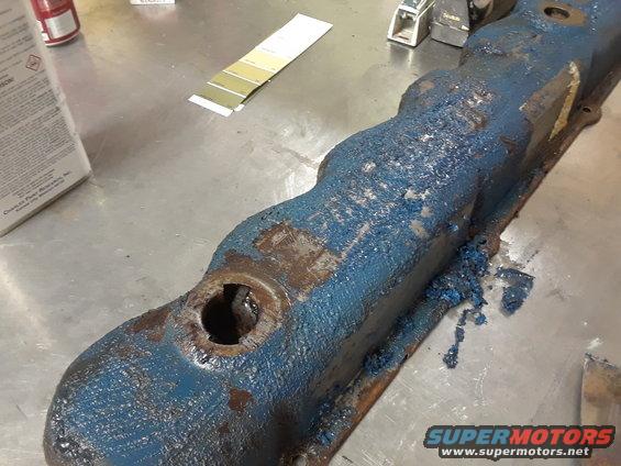 Old blue valve cover with rust and blue gunk on a metal table. Paint chip samples are nearby