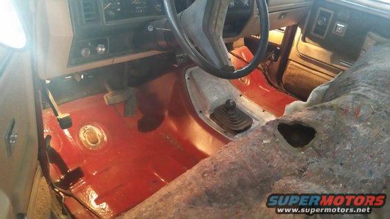 Interior of vehicle with red floor, exposed metal, and manual shifter