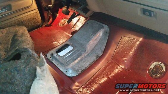 Interior floor console removed from a vehicle with red carpeting and a metal cover plate