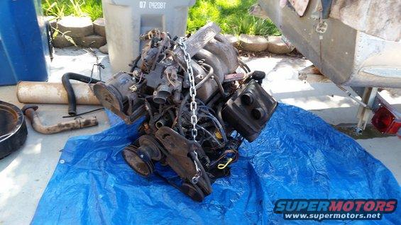 Engine on blue tarp with exhaust pipe and air filter housing nearby