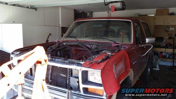 Maroon Ford Bronco in garage, hood open, engine out, engine hoist in front