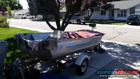 Aluminum boat with a red cover on a trailer in a driveway