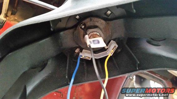 Close-up of a vehicle's headlight wiring harness with blue and yellow wires connected