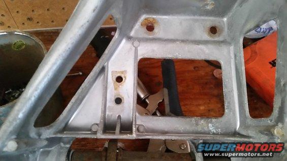 Aluminum bracket with holes and rust spots, on a wooden surface