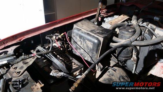 Engine bay with battery, hoses, and black plastic cover