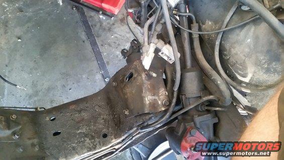 Rusty vehicle frame with hydraulic lines and steering components. A red object is visible at the bottom right