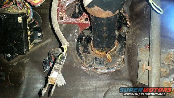Close-up of a vehicle's interior showing the steering column mount, wiring harness, and fuse box
