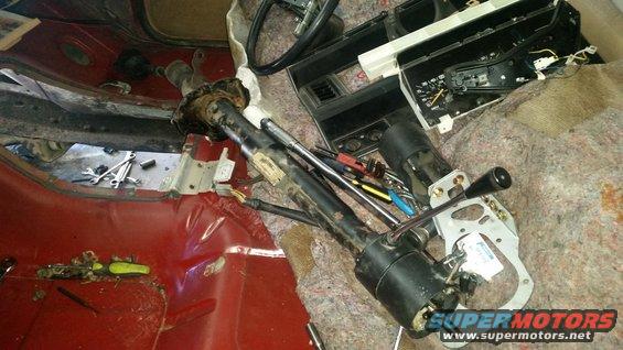 Disassembled steering column and dashboard parts in a red vehicle interior