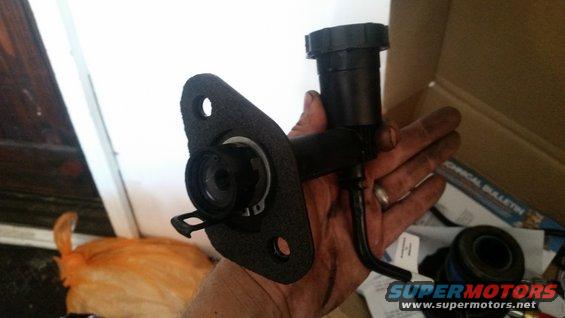Hand holding a clutch master cylinder assembly with a black reservoir and mounting flange