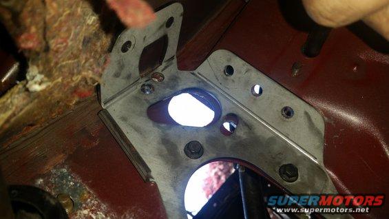 Metal bracket bolted to red car interior panel with visible insulation and holes