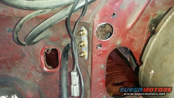 Red engine bay firewall with rust holes, wiring, and brass fittings