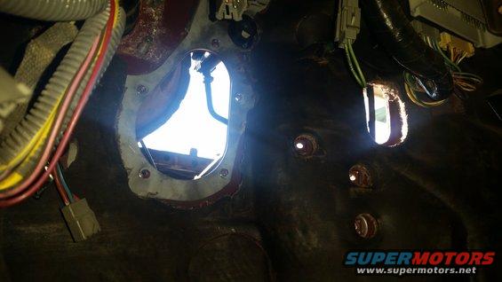 Vehicle firewall interior with large circular opening, smaller rectangular opening, wiring harnesses, and Supermotors logo