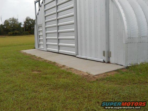 Side view of a large metal Quonset hut building with a concrete ramp leading to its sliding doors