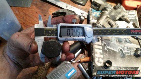Digital caliper measuring a bolt on a workbench with tools and a diagram of a pickup truck